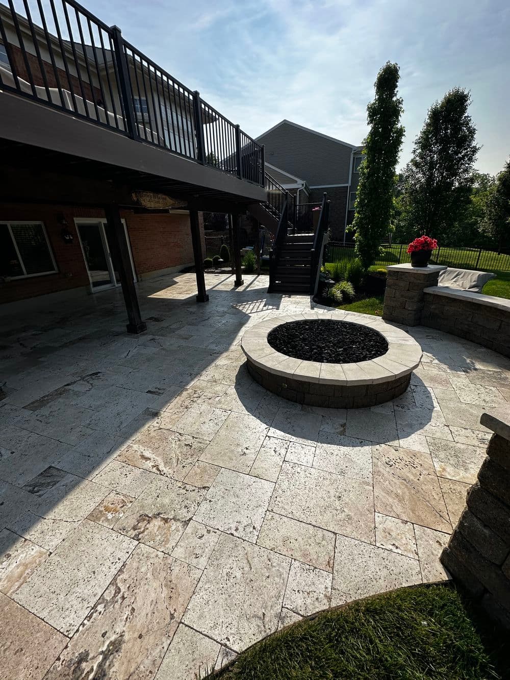 Patio with stone fire pit, landscaped yard, and wooden deck in sunny residential setting.