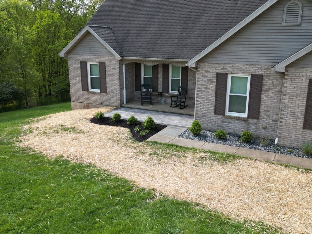 Front yard of a home with straw landscaping, flower beds, and a porch seating area.