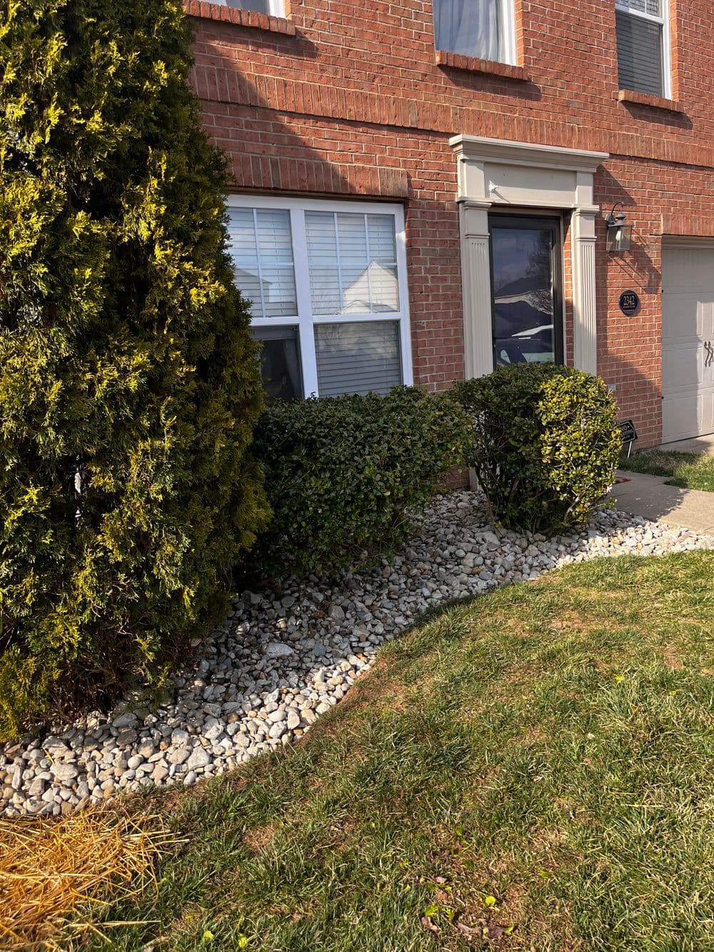 Brick house exterior with landscaped garden, featuring shrubs, stones, and green grass.