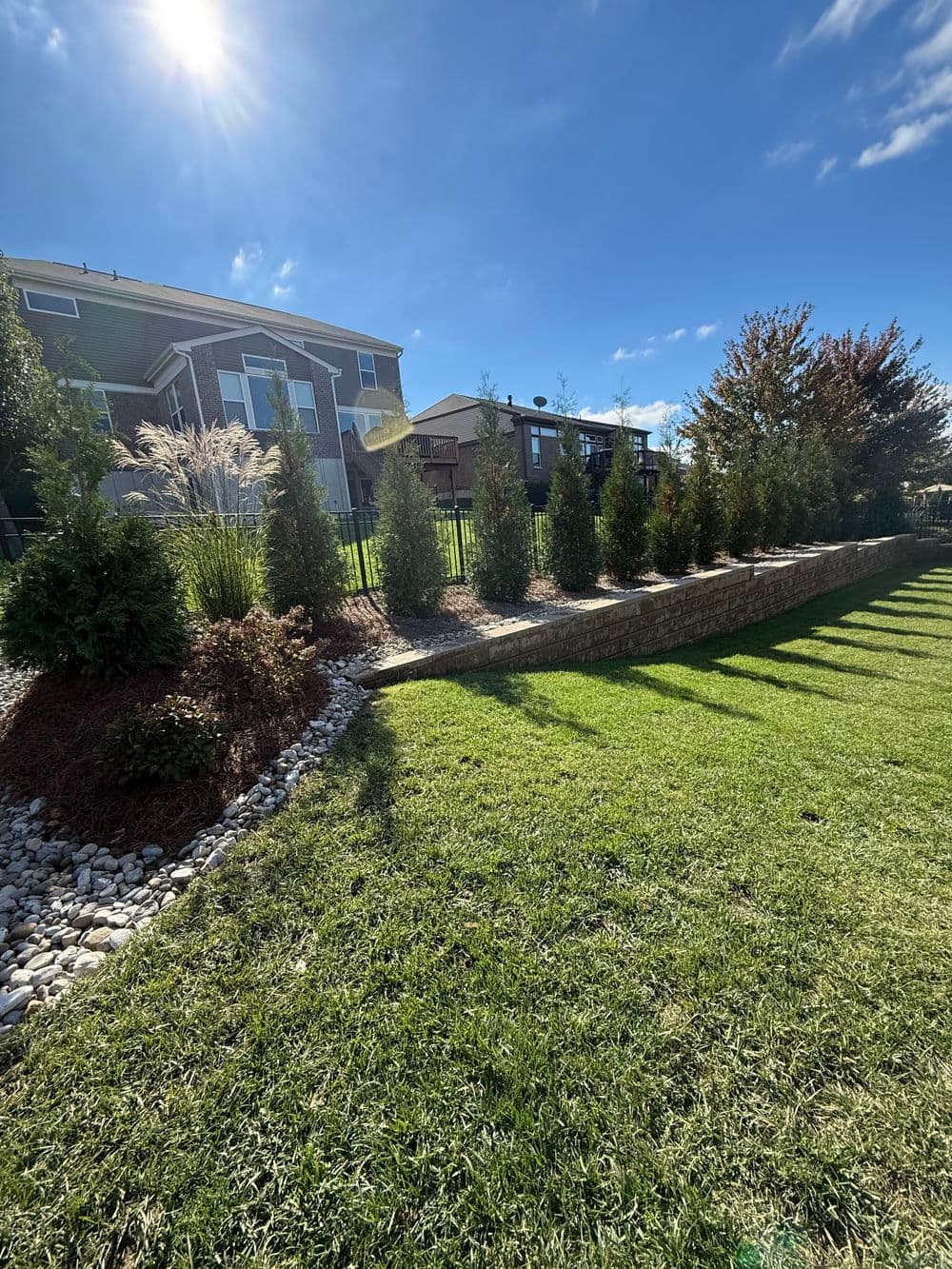 Lush green lawn with landscaped hedges and stone border under a clear blue sky.