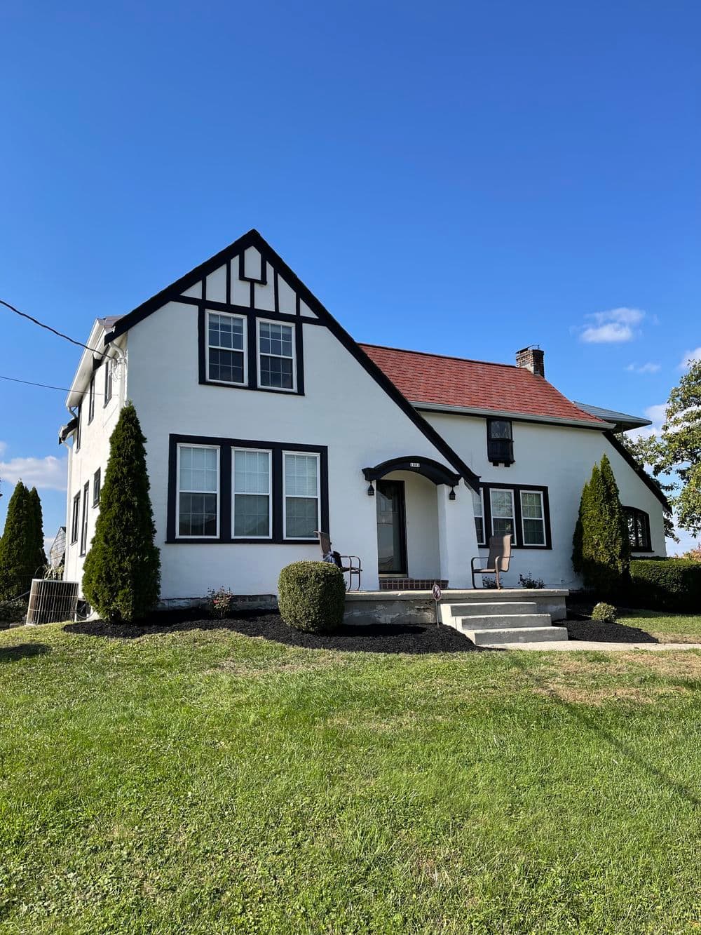 Charming white house with Tudor accents, green lawn, and clear blue sky. Ideal suburban setting.